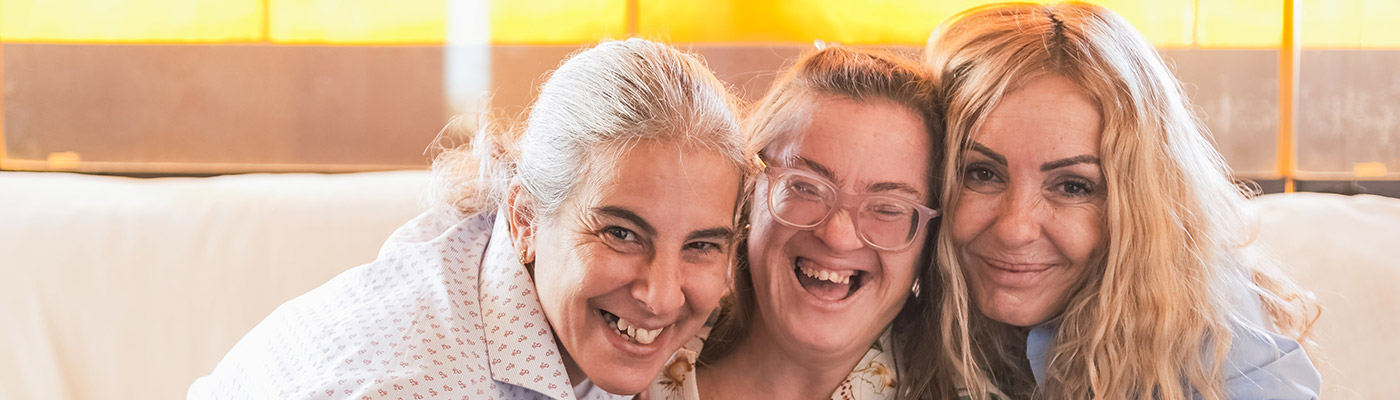 Tres mujeres sentadas juntas en un sofá sonríen y se apoyan mutuamente.