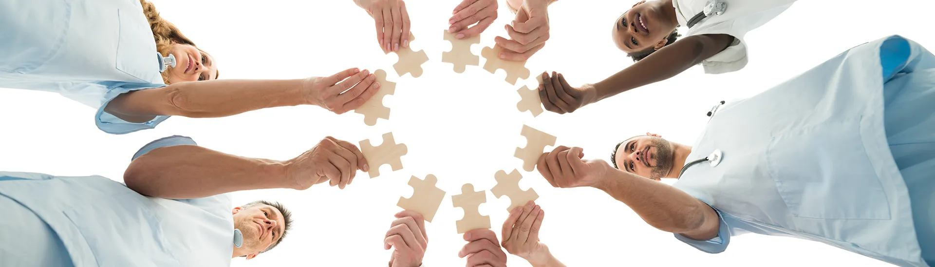 A group of medical professionals holding puzzle pieces in a circle with the camera in an upward facing angle to capture the shot.