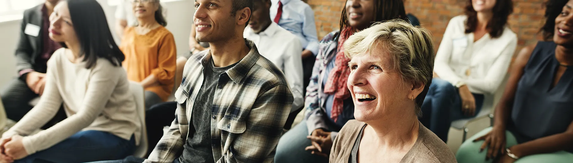 A group meeting of different men and women sitting, listening to a presenter.