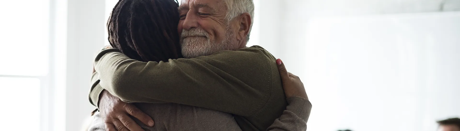 Man hugging woman with dreadlocks with a warm smile on his face in a moment of happiness.