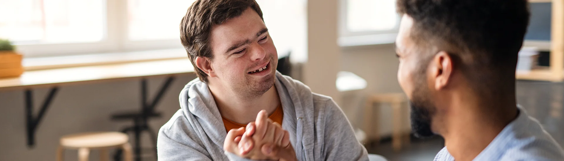 Happy man with down syndrome shaking hands with a friend in classroom.