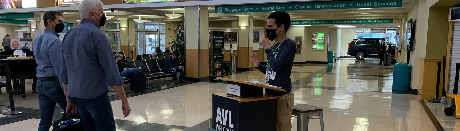 Two men being greeted as they are walking through Asheville regional airport wearing masks.