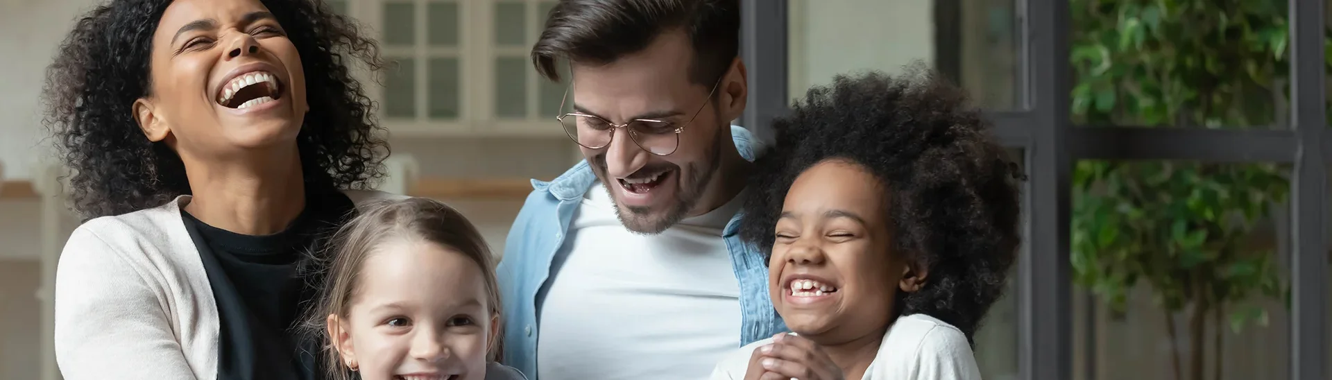 Multiracial family of four laughing excitedly together on a couch