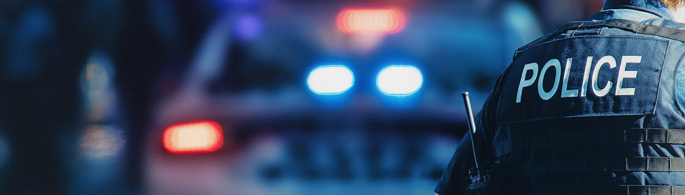 Police officer in front of police car with lights on