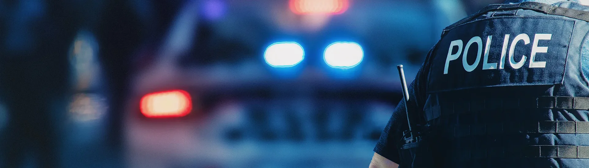 Police officer in front of police car with lights on