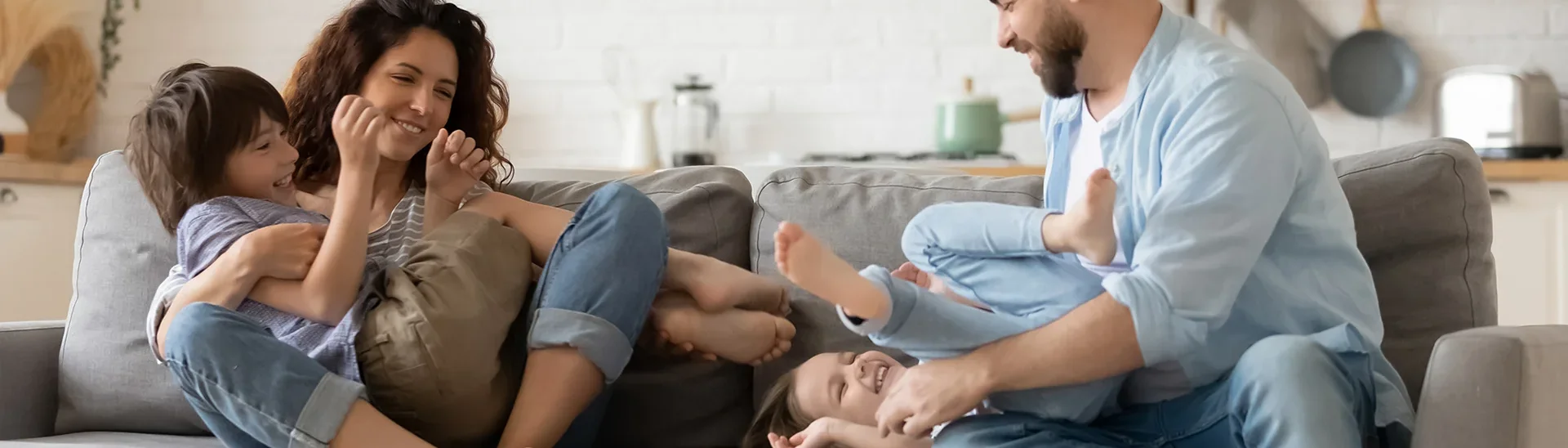 Una familia feliz riendo en el sofá. El padre hace cosquillas a la hija y la madre abraza al hijo.