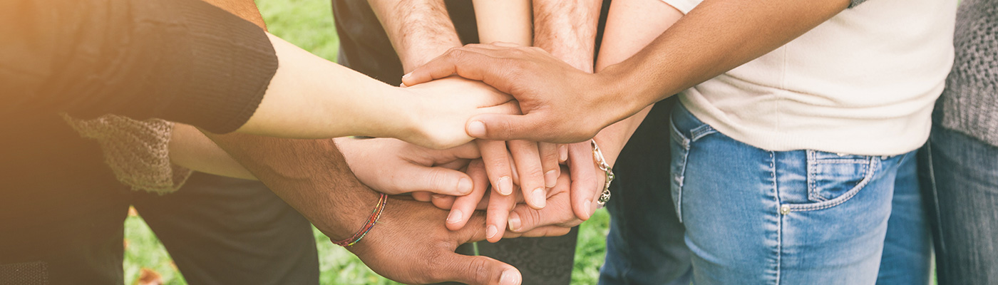 Several people of different ethnicities standing in a circle with their hands on top of each others.