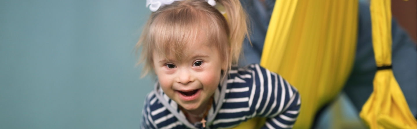 Young girl with down syndrome smiling happily, wearing a blue and white striped shirt.