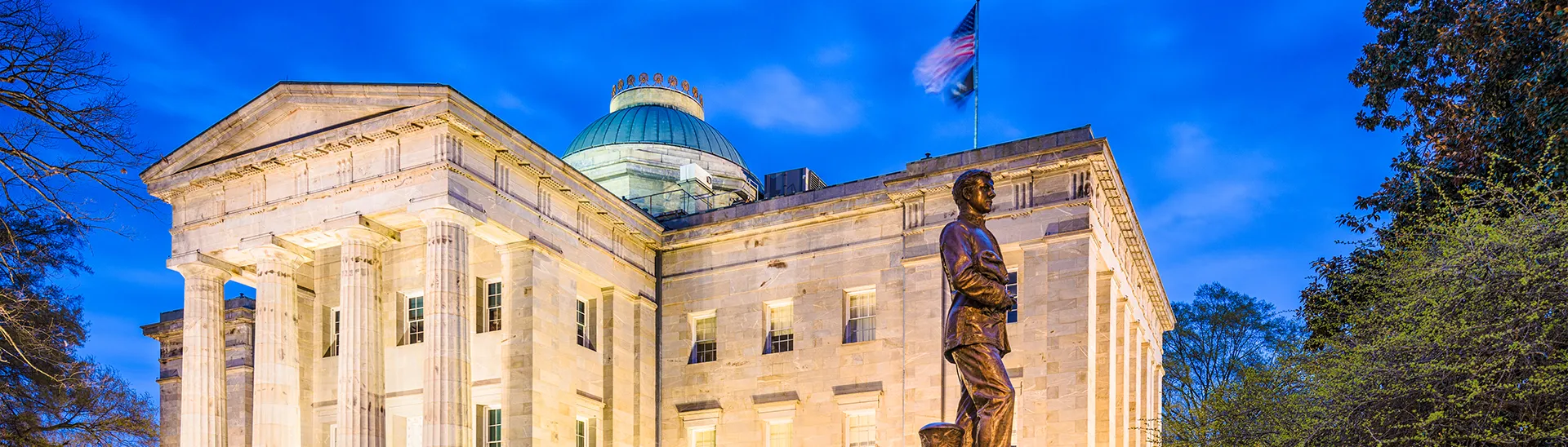 North Carolina capital building with statue out in front of it with the picture taken in the early evening.