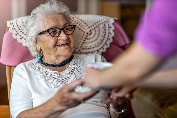 Una anciana recibe ayuda de un cuidador con una sonrisa en la cara.